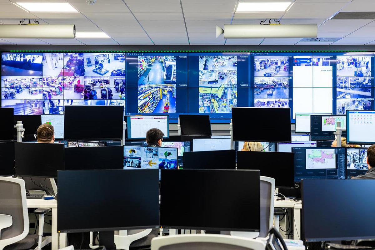 Various people working at desks with a wall of computer screens in front of them, 显示了一系列闭路电视图像